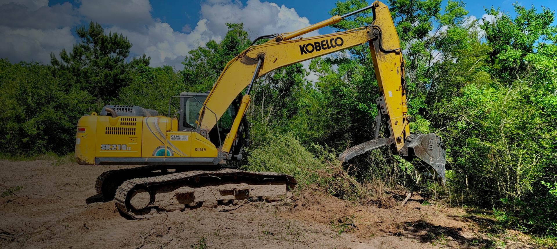 Yellow excavator clearing land by trees